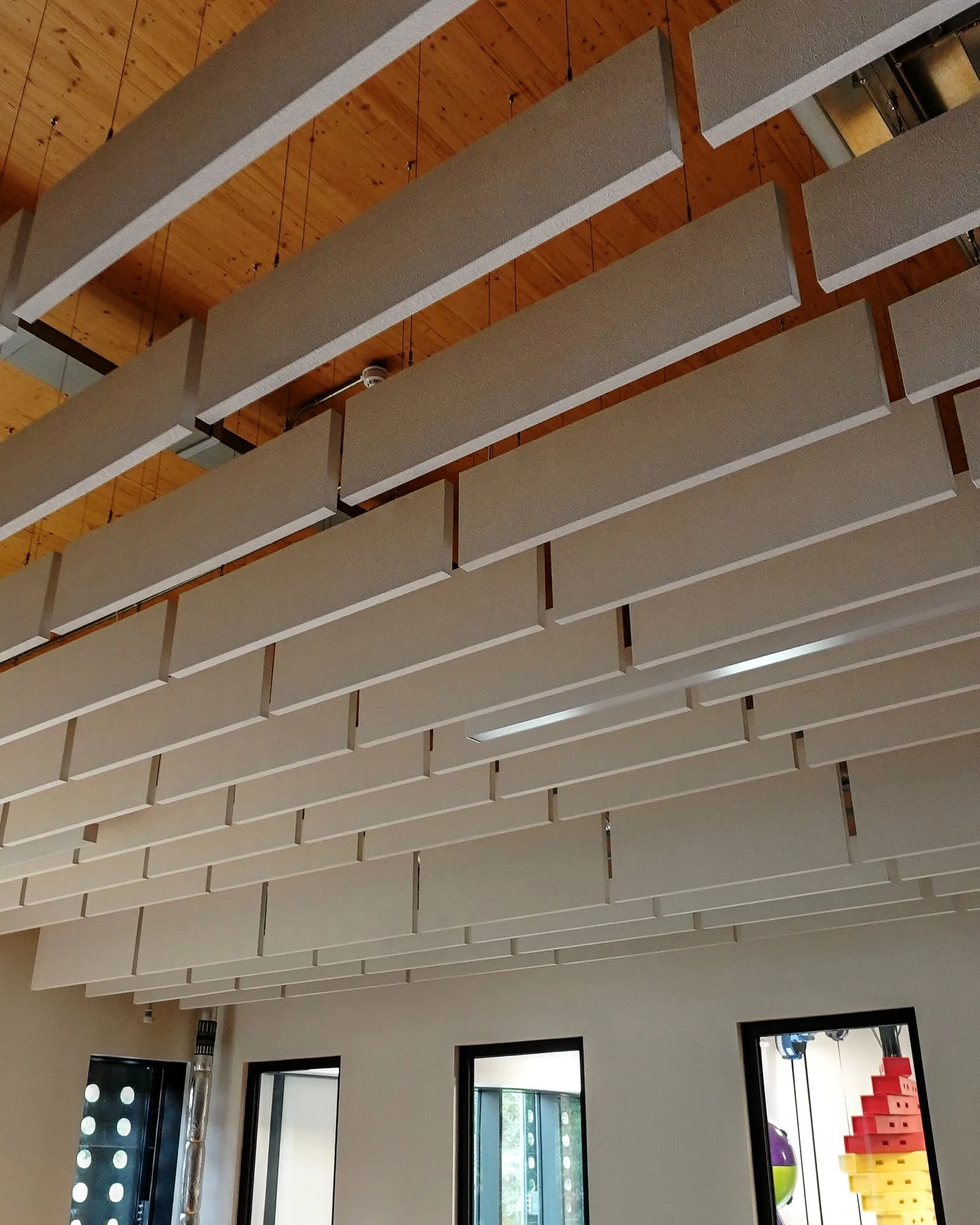 Rows of white acoustic baffles hanging under the timber roof of a studio at Spelthorne Leisure Centre