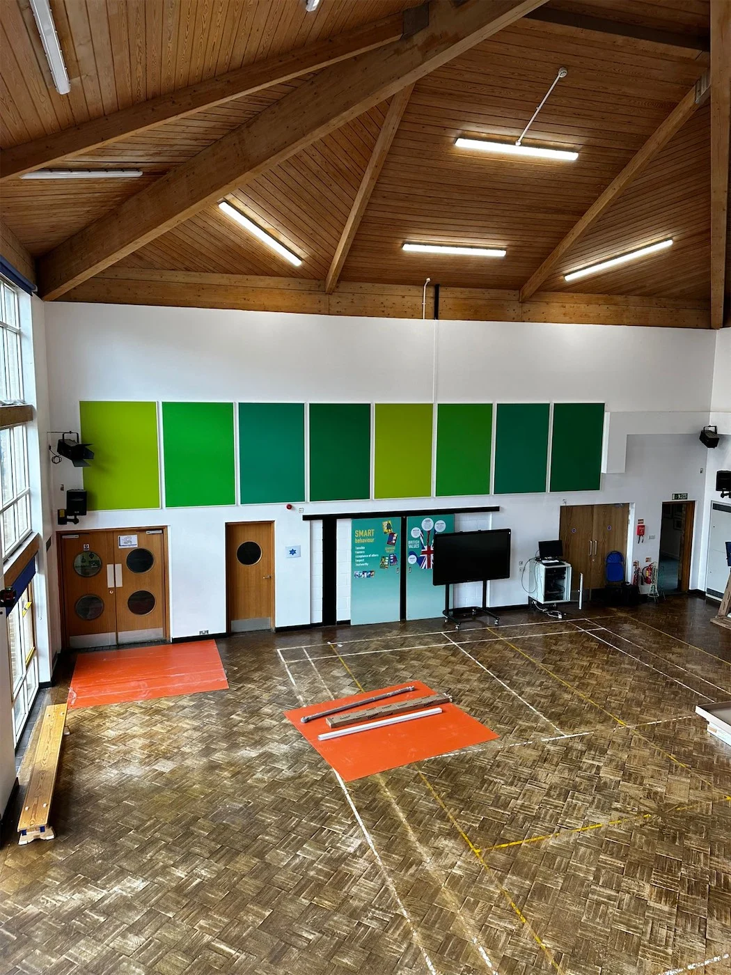 School hall with graded green acoustic wall panels below a timber vaulted roof